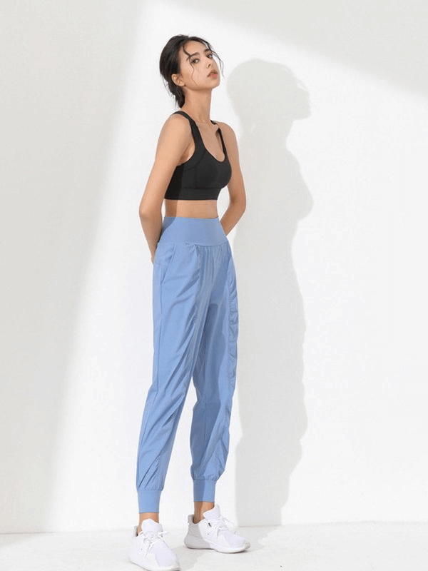 Woman wearing lightweight blue sports pants with a wide belt and cuffs, perfect for yoga and mobility, paired with a black top and white sneakers.